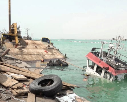 A partially sunken boat lists near a debris-strewn dock after strikes on Mocha, Yemen A partially sunken boat lists near a debris-strewn dock after strikes on Mocha, Yemen