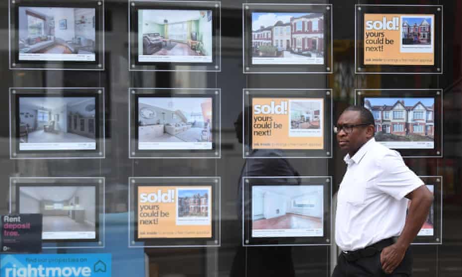 A person passes properties advertised at an estate agent in London, Britain.