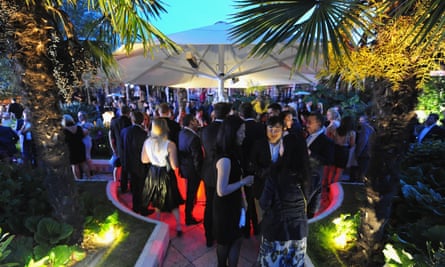 A crowded open-air party, with people talking under gazebos and floodlit palm trees