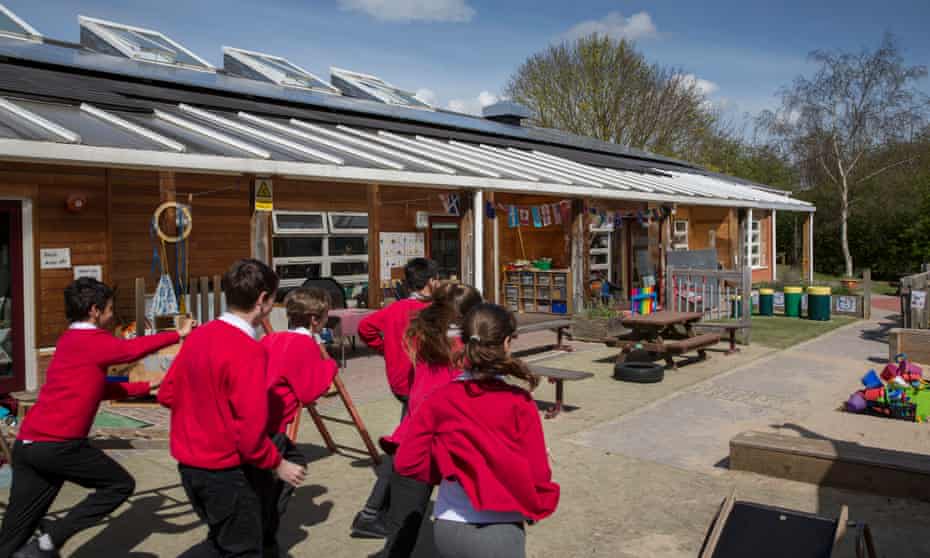 Primary school children in red uniforms run outside in their playground