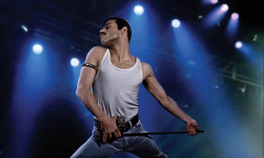 Rami Malek in a white vest and jeans, striking a classic Freddie Mercury pose