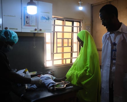 Azuwaira looks down at Hambali, who is lying on a table, surrounded by two medical workers