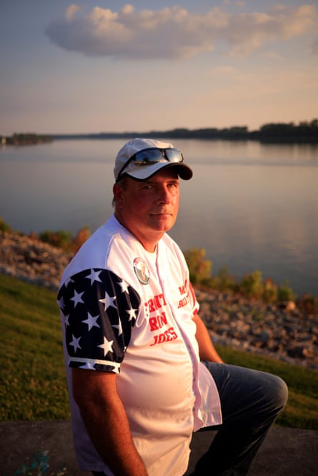 A middle-aged man with an US flag-inspired shirt at the banks of a river.