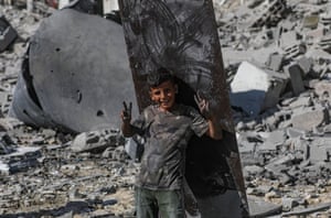A boy, smiling and making the peace sign with his hands, standing amid rubble