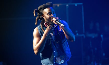 A person wearing a denim vest sings into a microphone onstage