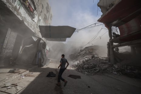A person walks through smoke past rubble from an Israeli strike in the Al-Shati refugee camp in Gaza