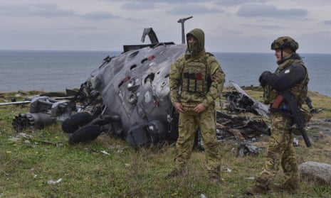Ukrainian soldiers stand against the background of a damaged Russian military helicopter on Snake Island.