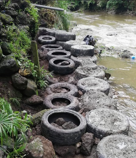 A line of car tyres filled with dirt along a riverbank