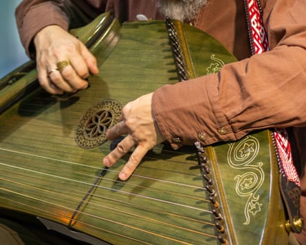 Closeup of hands plucking strings on a decorated wooden psaltery instrument