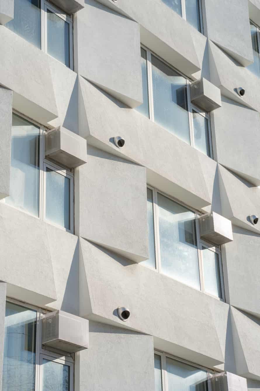Close up image of a white multi-story building facade with angular rectangular panels around its windows.