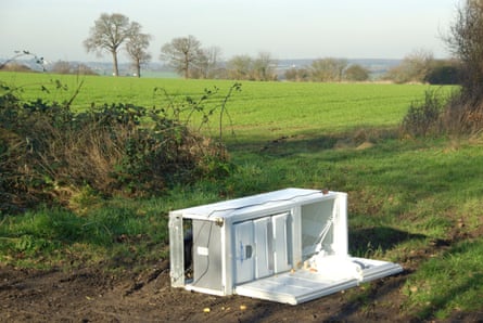 A dumped fridge freezer lies at the edge of a green field