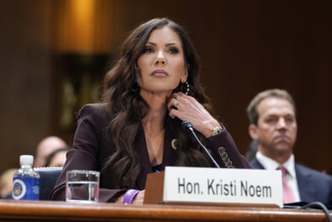 Kristi Noem testifies at a Senate hearing desk, her husband seated behind her