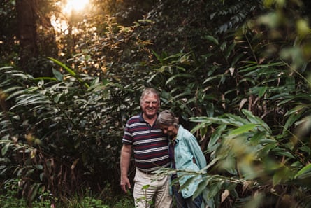 An older couple standing shoulder to shoulder and laughing in a forest as the sun sets behind them