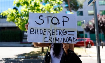 a woman holds a sign that reads 'stop bilderberg criminals'
