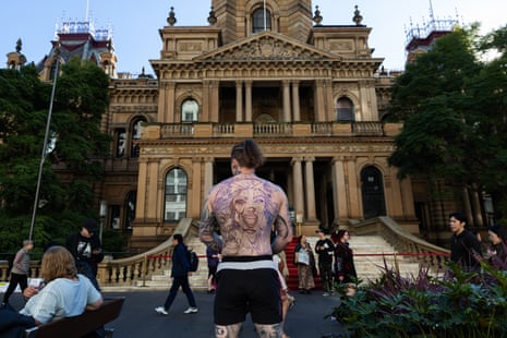 Pauly stands in front of the town hall with his shirt off and tattooed back to camera