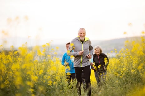 Group of active seniors running together outside on the meadow full of flowers. Front view