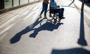 A caregiver pushes a man in a wheelchair on footpath