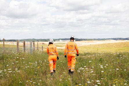Two HS2 workers walk away from the camera on chalk grassland.