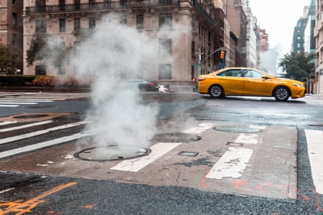Steam rises from a New York manhole on a wet street as a yellow taxi drives past