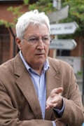 A man with white hair and glasses gestures while speaking.