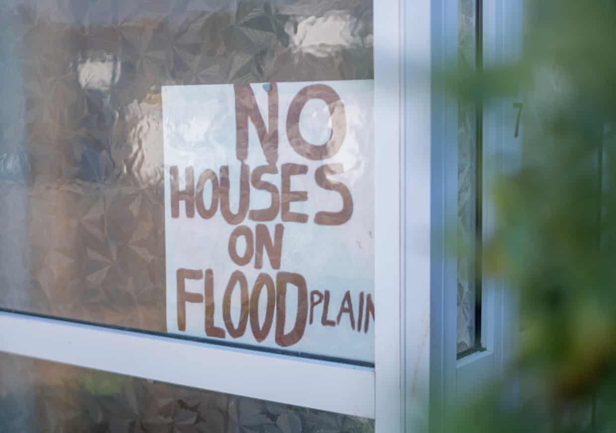 A sign in the window of a home says ‘No houses on flood plain’.