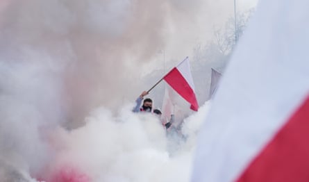 A masked man seen through smoke waving a Polish flag