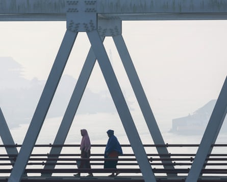 Two people walk across a bridge with the natural landscape behind them obscured by a thick white smog