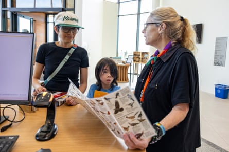 A woman and boy talk to another woman who is holding a foldout information pamphlet on birds.