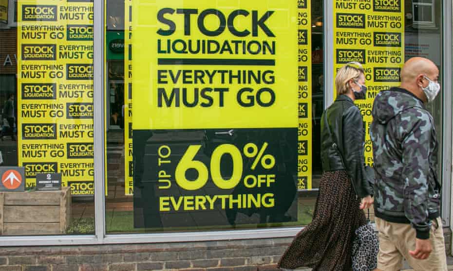 Two people walk past yellow and black signs in a shop window promoting discounts of up to 60% off