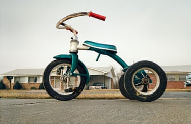 A photograph of a bike with high handlebars and a blue saddle and a one-story building behind it