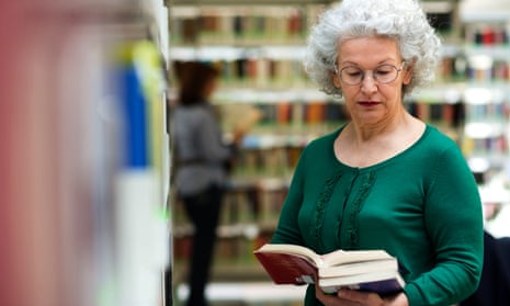Portrait of older retired woman choosing book in library and taking it from shelf.