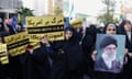 Iranian women wearing headscarves and black hooded robes hold signs and a portrait of the supreme leader, Ayatollah Ali Khamenei: the signs read Down With USA and Down With Israel