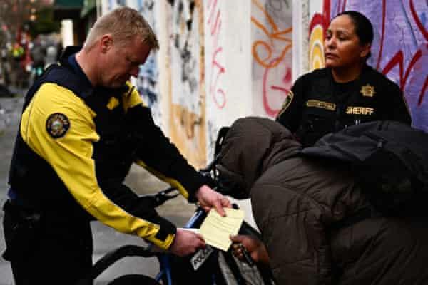 Man wearing yellow ‌and black holds out paper to⁤ person in black jacket