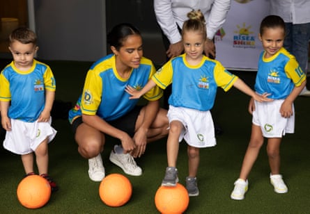 Mary Fowler crouches next to three children with soccer balls