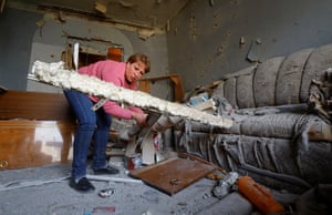Woman wearing pink top next to ripped sofa in damaged building