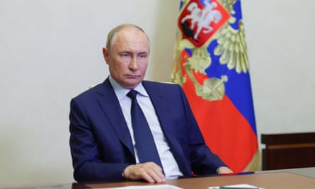Vladimir Putin sitting at a desk by a Russian flag