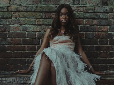 John Glacier sitting against a brick wall in a feather-detail gown