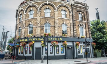 Street view of the Royal Vauxhall Tavern, a pub on the bottom floor of an old brick building with flower baskets and event posters hanging on the facade