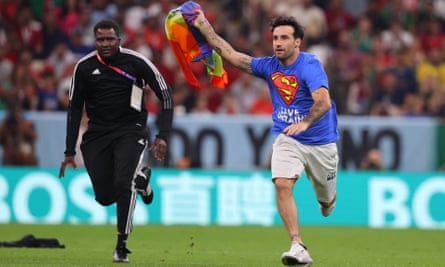 A protester is chased by security while holding a rainbow flag and with a shirt saying “Respect For Iranian Women” on his back.