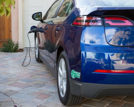 Plug-in electric car with carpool sticker parked in driveway, with connector plugged in and charging at home