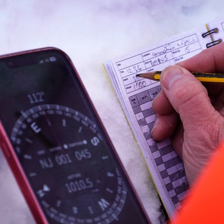 A compass next to a hand holding a pencil writing data in a book
