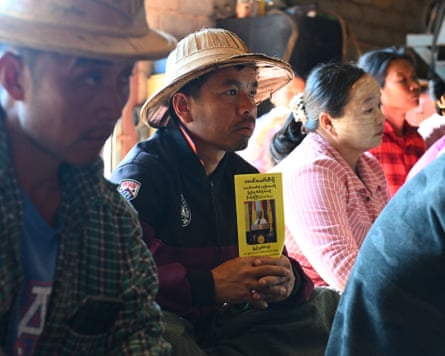 A man sitting in a crowd holding a yellow pamphlet