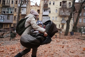 A woman carries her child as they evacuate from a residential building which was hit by a Russian rocket in the city centre of Kharkiv