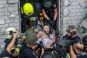A man covered in brick dust is carried from a building by rescue workers