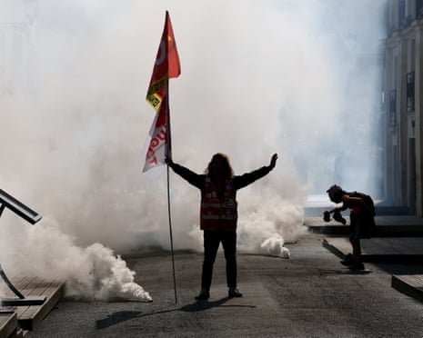 A protester with a large flag stands with arms outstretched in a cloud of teargas