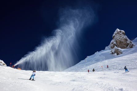 A snowcape against a deep blue sky with snow projecting from a small cannon-like machine