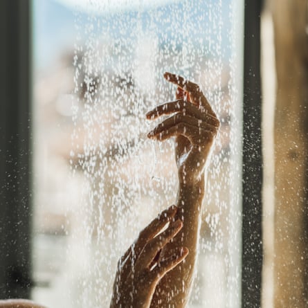 Mãos de mulher fecham sob gotas de água do chuveiro.