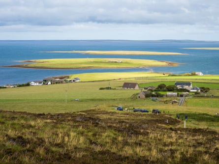 Looking over moorland and green fields to the sea in Orkney with crofts in the foreground and islands out at sea
