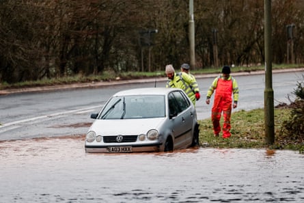 Workers assess the situation near an abandoned car in flood water near Fenny Bridge in Ottery Saint Mary.