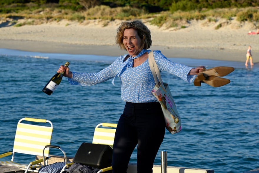 Sally Phillips håller en flaska vin och sina skor, på en båt vid stranden, f